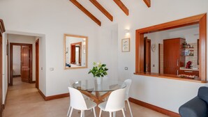 A modern kitchen with a glass dining table, white chairs, wooden beams, and a blue sofa.
