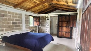 Un dormitorio con cama, techo de madera, pared de ladrillo y puerta que da a otra habitación.