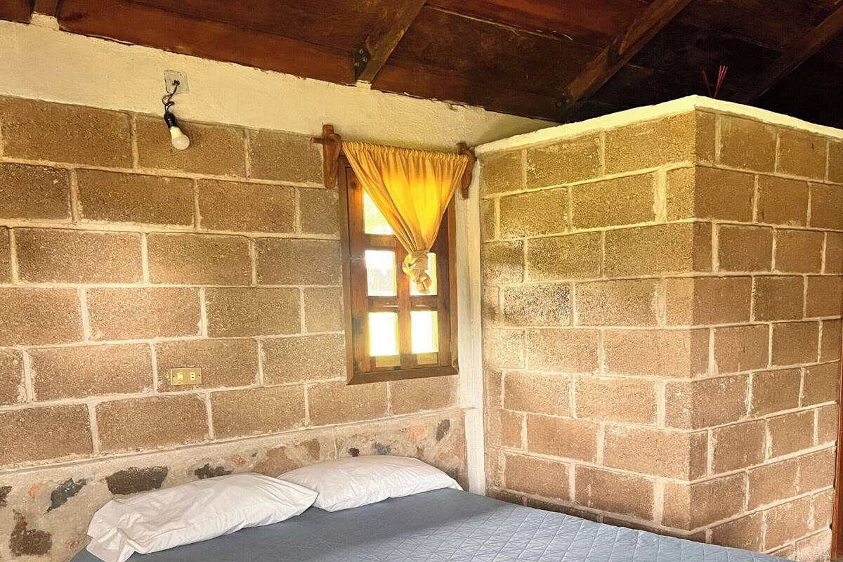 Una cama individual con un edredón azul en una habitación con paredes de piedra y techo de madera.