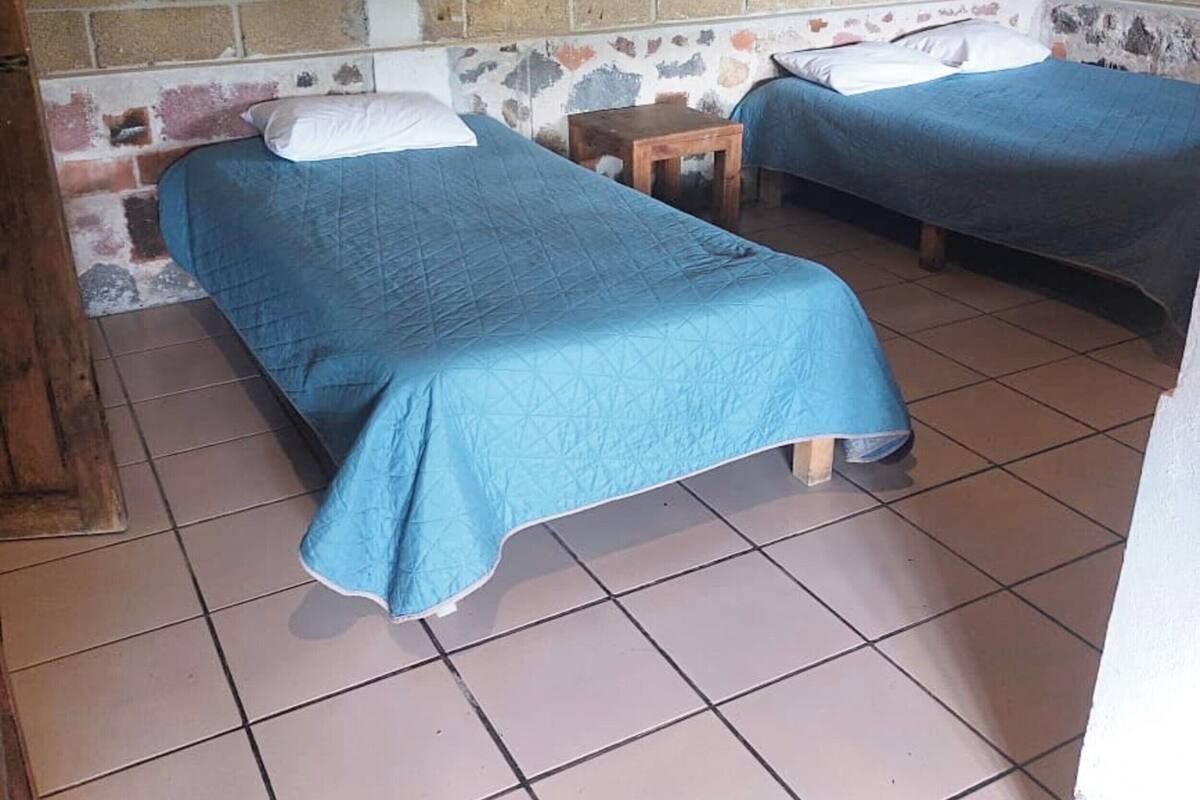 Una habitación con dos camas, una mesita de madera y una pared de ladrillo.