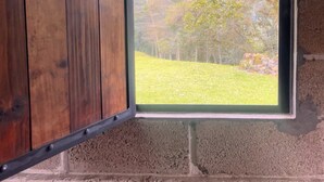 Una habitación rústica con una puerta de madera y una ventana que da a una zona con césped y árboles.