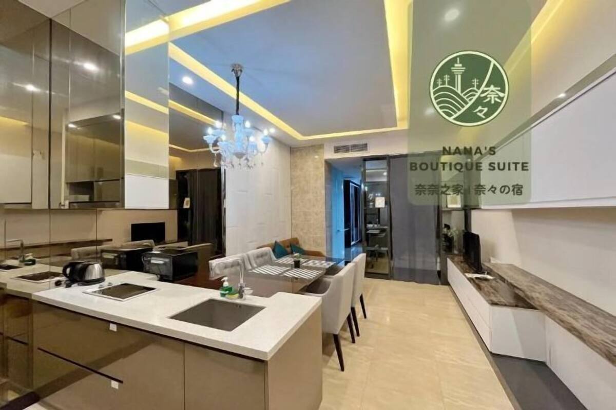 Eine moderne Küche mit einer zentralen Kochinsel, einem Essbereich mit Tisch und Stühlen sowie dem sichtbaren Logo von 'NAMA'S BOUTIQUE SUITE'.