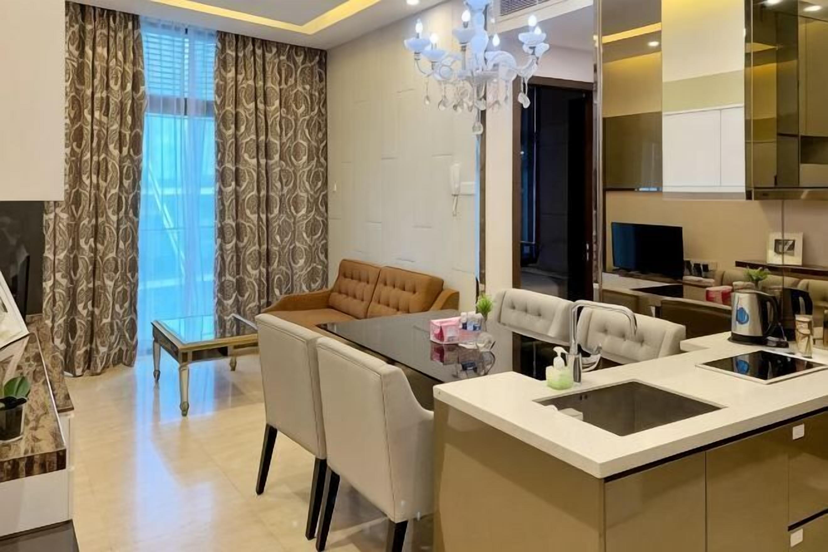 A modern kitchen with a dining area, a chandelier, and a large window with curtains.