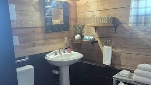 Une salle de bain avec des murs en bois, un lavabo sur colonne, des toilettes et une petite étagère avec des serviettes.