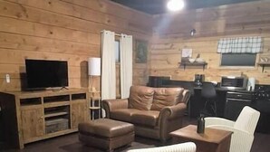 Un salon chaleureux avec un mur en bois, un canapé, un fauteuil à rayures, une table basse et un téléviseur à écran plat.