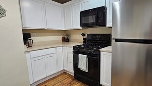 A kitchen with white cabinets, a black stove, a stainless steel refrigerator, and a microwave.