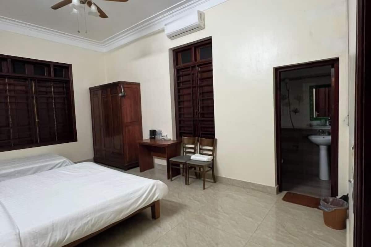 A bedroom with two beds, a desk, a chair, a wardrobe, and a bathroom visible through an open door.