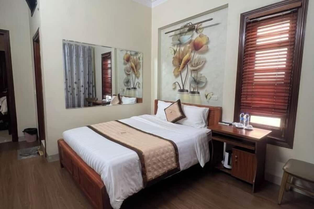 A bedroom with a bed, a desk, a chair, and a window with blinds.