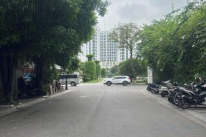 Una strada con auto e motociclette parcheggiate, alberi lungo il marciapiede e un edificio sullo sfondo.