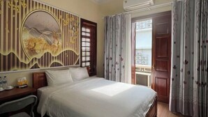 A hotel room with a bed, a desk, a chair, a decorative wall, and a window with curtains. - HOANG HA VILLA (Bac Ninh)