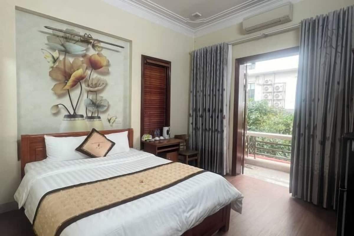 A hotel room with a bed, a desk, a chair, a window with curtains, and a balcony.