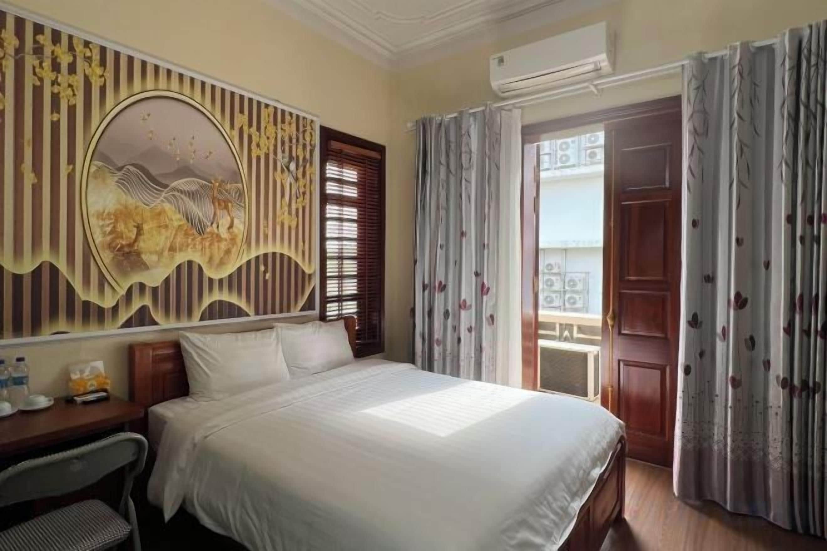 A hotel room with a bed, a desk, a chair, a decorative wall, and a door.