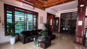 A lobby with a leather sofa, glass coffee table, potted plants, and wooden ceiling beams. - HOANG HA VILLA (Bac Ninh)