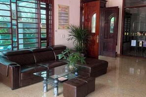 A lobby with a leather sofa, a glass coffee table, and a potted plant. - HOANG HA VILLA (Bac Ninh)