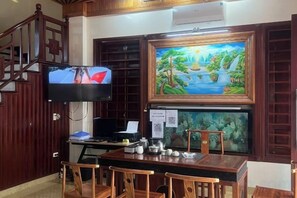 A room with a wooden desk, chairs, a television, a painting, and an aquarium. - HOANG HA VILLA (Bac Ninh)