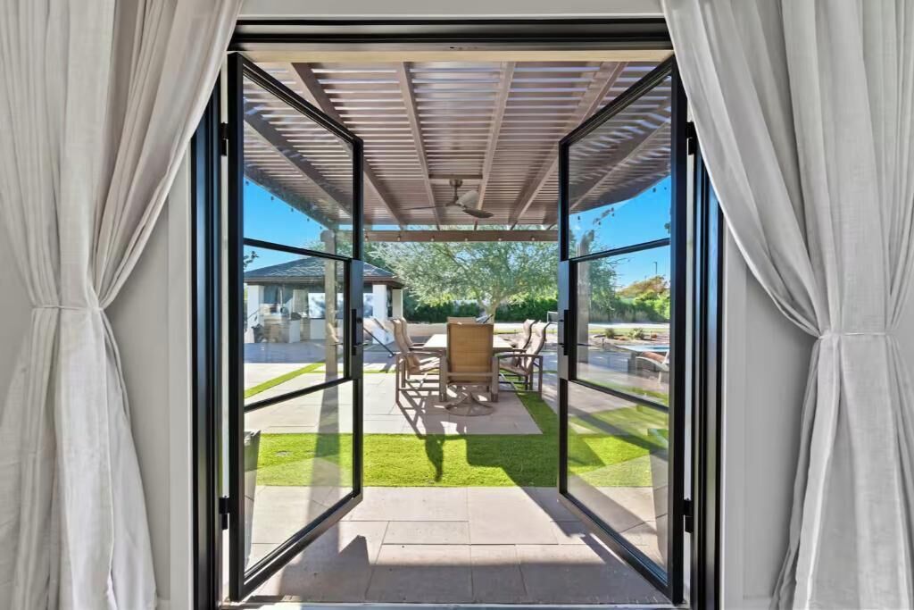 An open sliding glass door leading to an outdoor patio area with a pergola, seating, and a lawn.