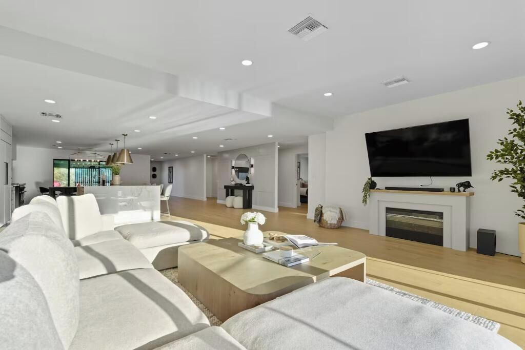 A modern living room with a large flat-screen TV, a fireplace, and a dining area in the background.