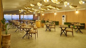 Un comedor amplio con varias mesas y sillas, grandes lámparas colgantes y vistas a través de amplios ventanales.