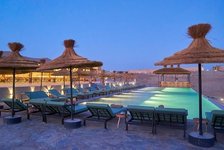 A poolside area with lounge chairs and thatched umbrellas, surrounded by a desert landscape.