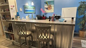 A kitchen with a bar area, featuring a microwave, a coffee maker, and a sink. There are two bar stools and a potted plant. - Great room w/ pool table in a 1-bdrm party barn in Newaygo; River access (Newaygo)