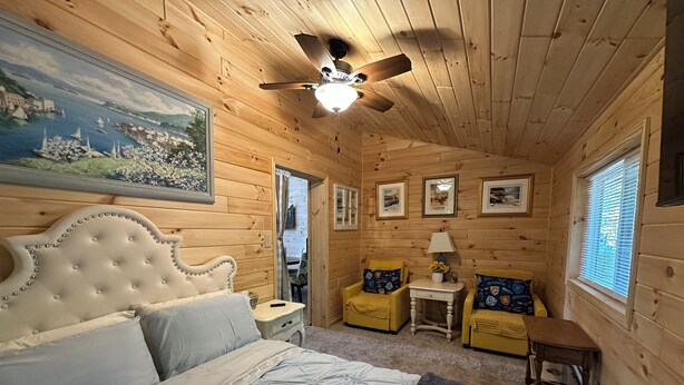 A wooden cabin bedroom with a bed, a ceiling fan, framed pictures, and a window. - Great room w/ pool table in a 1-bdrm party barn in Newaygo; River access (Newaygo)