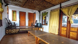 A room with a wooden floor, a long table, two wooden doors, a television, and a window with curtains. - ARBA Artana & Chipsari Hotel Pangalengan (Pangalengan)
