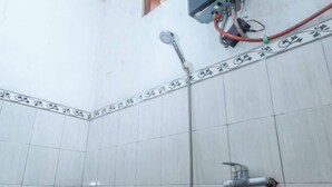 A bathroom with white tiled walls, a shower area, and a visible electrical outlet with a red cable. - ARBA Artana & Chipsari Hotel Pangalengan (Pangalengan)
