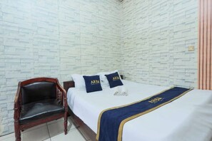 Ein Hotelzimmer mit einer Wand im Backstein-Muster, einem Holzbstuhl, einem Bett mit blauer und goldener Bettdecke und zwei Kissen mit einem Logo.
