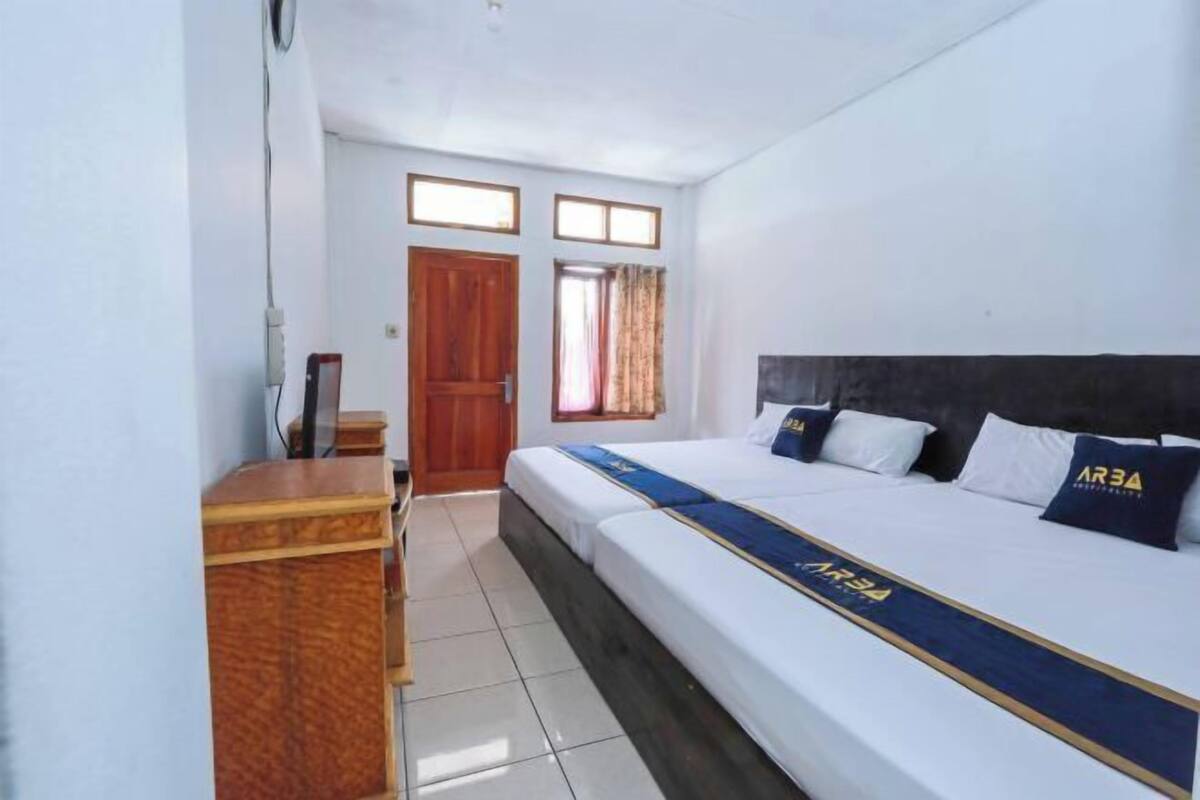 A hotel room with a bed, a wooden desk, a window, and a door.