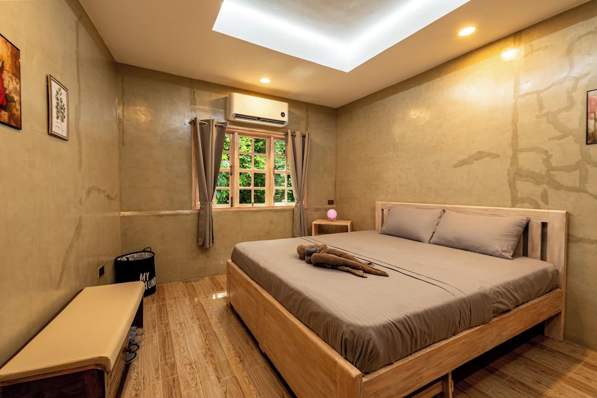 A bedroom with a skylight, a bed, a bedside table, a bench, and a window with curtains.