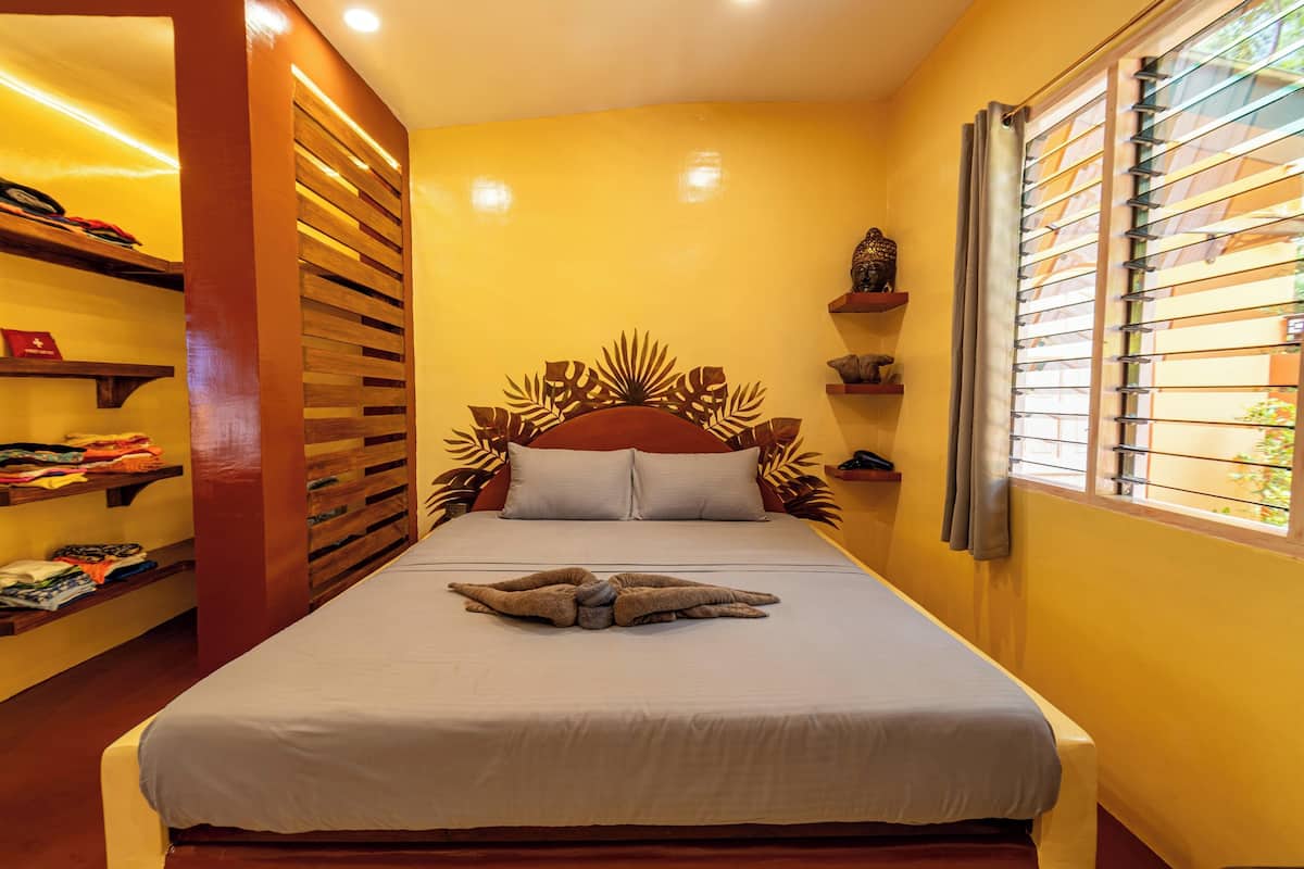 A hotel room with a bed, wooden headboard, and a window with blinds.