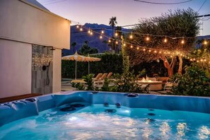 Un bain à remous avec un espace aménagé au bord de la piscine, des guirlandes lumineuses et des chaises longues.
