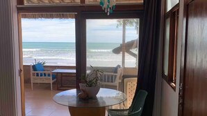 Una habitación con mesa de vidrio, dos sillas, vistas a la playa y un ventilador de techo.