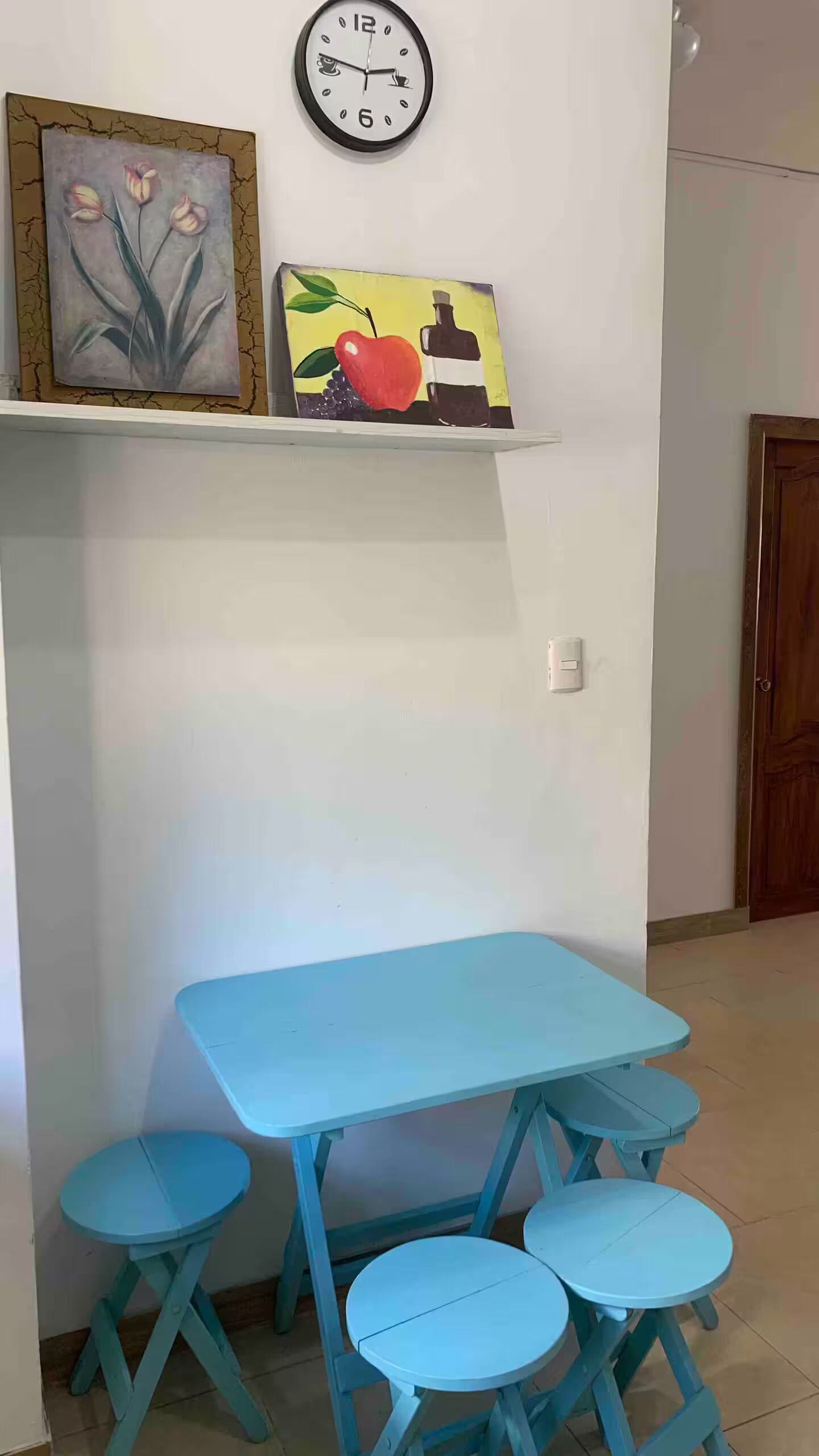 Une pièce avec une table bleue et quatre tabourets assortis, une horloge murale et deux tableaux encadrés.