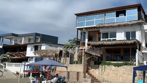 Un edificio de dos pisos con techo de paja, ventanas grandes y una escalera que conduce al nivel superior.