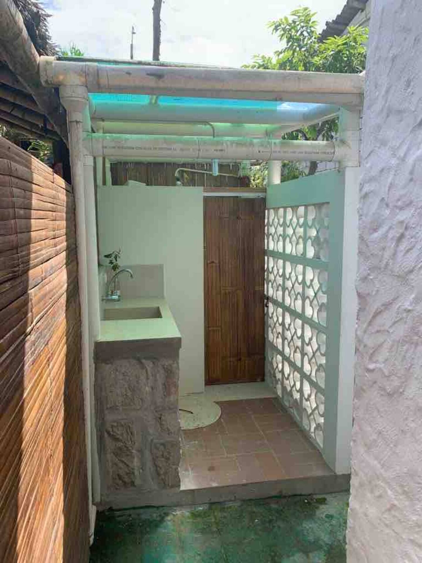 Een kleine, afgesloten badkamer met een stenen wastafel, een houten deur en een decoratieve metalen scheidingswand.