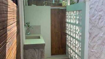 Een kleine, afgesloten badkamer met een stenen wastafel, een houten deur en een decoratieve metalen scheidingswand.