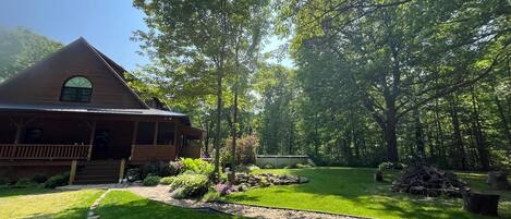 A rustic cabin with a porch, surrounded by lush greenery and a well-maintained lawn.