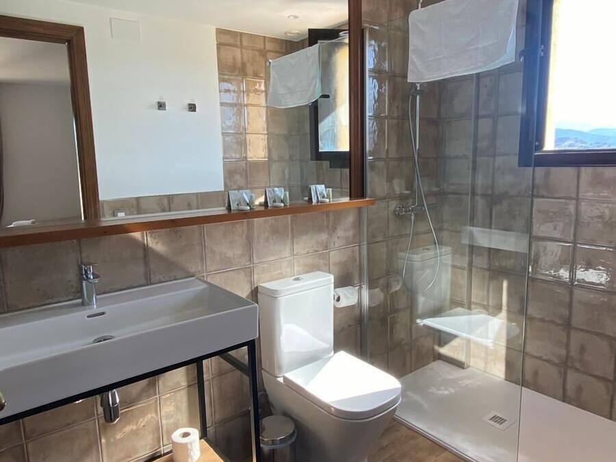 Un baño moderno con un espejo grande, un lavamanos, un inodoro y una ducha con cerramiento de vidrio.