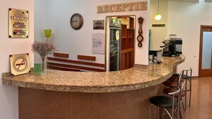 Een hotel receptie met een granieten balie, een klok, een agenda en een koffieapparaat.