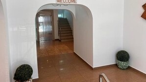Een modern interieur met een 'WELCOME' bord, een trap en twee potplanten.