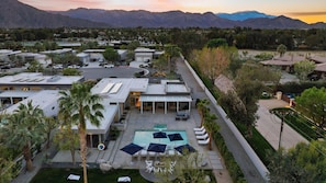 A modern resort with a swimming pool, lounge chairs, and a view of mountains.