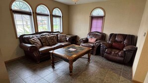 A spacious living room with a brown leather sofa, a matching armchair, and a wooden coffee table. There are large windows with arched tops, a ceiling fan, and a tiled floor. - Charming 1-bedroom house in enjoyable Milan with AC (Milan)