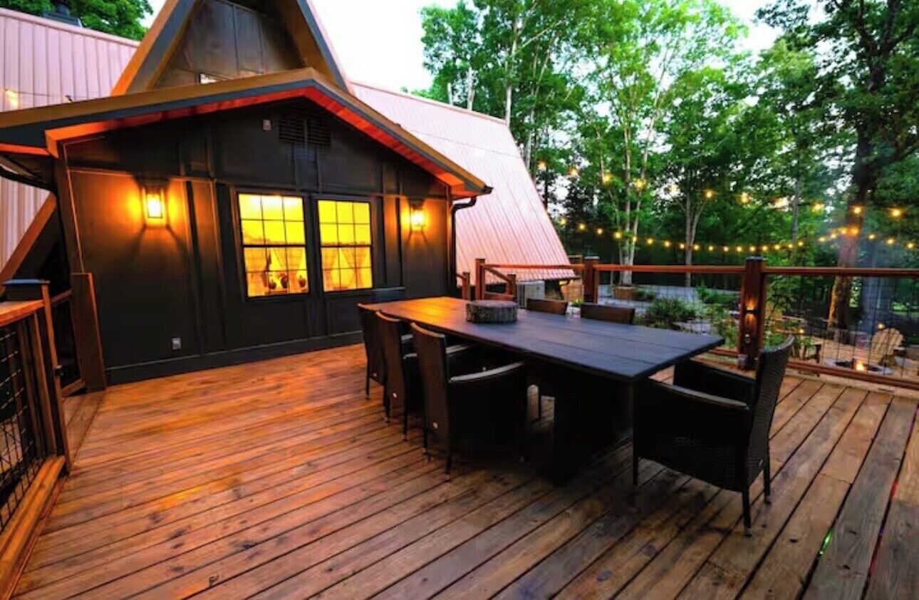 A wooden deck with a dining table and chairs, a small building with a sloped roof, and string lights.