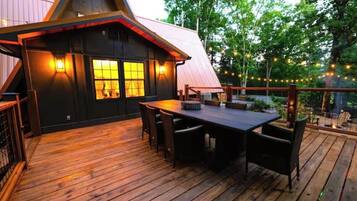 A wooden deck with a dining table and chairs, a small building with a sloped roof, and string lights.