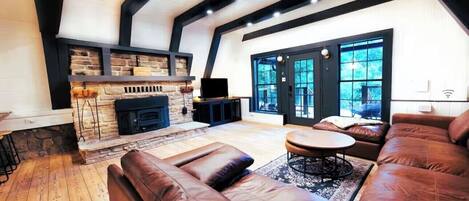 A modern living room with a stone fireplace, leather sofas, and a large window offering a view of the outdoors.