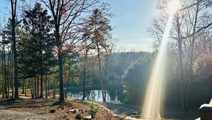 A serene lakeside setting with a wooden deck overlooking the water, surrounded by trees and a stone pathway. - Gorgeous A Frame on 18 private acres.  (Oneonta)