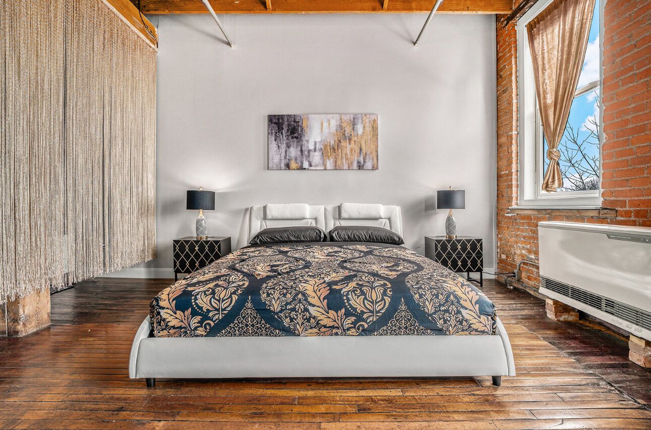 A bedroom with a large bed, two bedside tables with lamps, a radiator, and a brick wall.