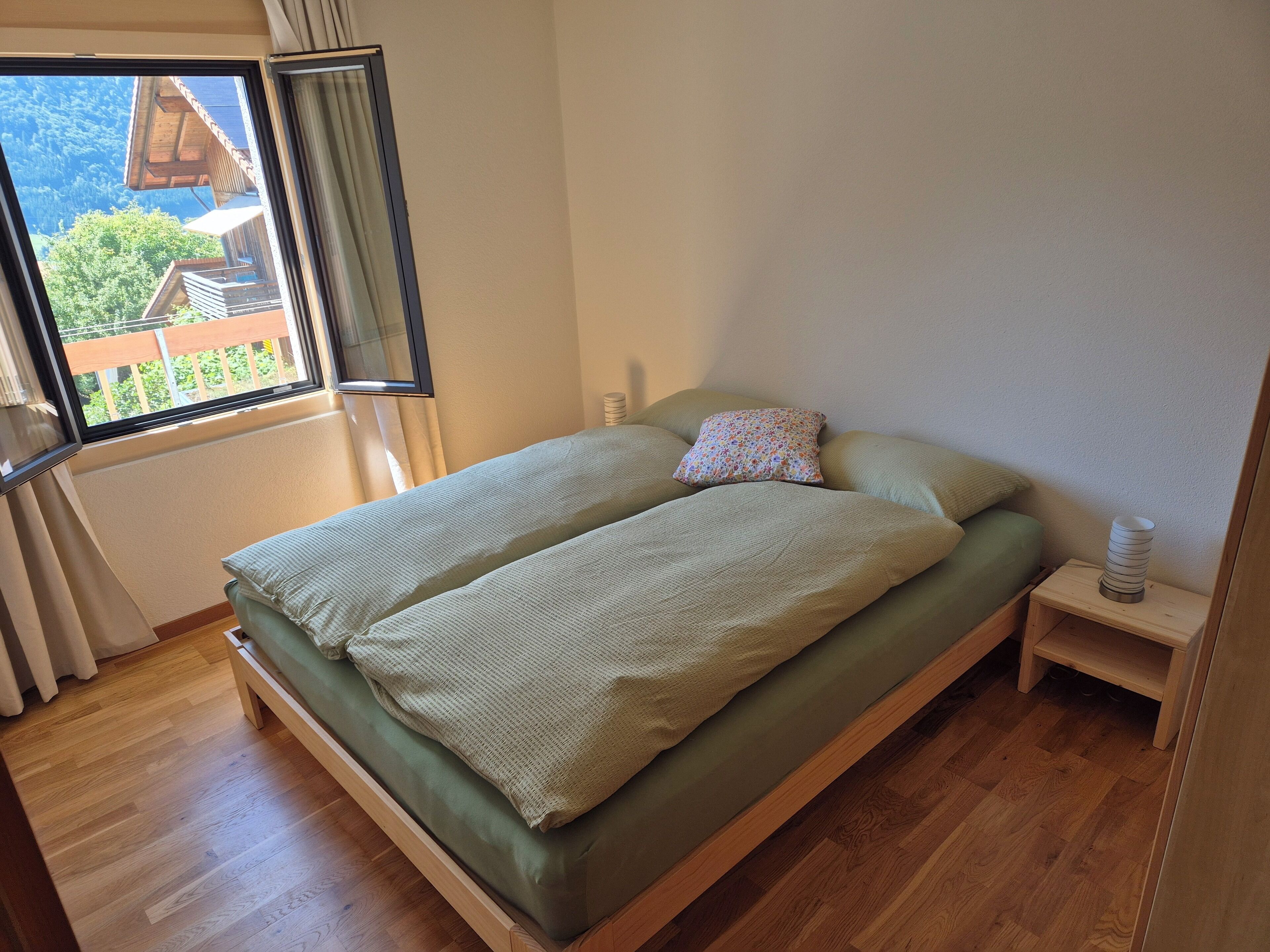 Une chambre avec un lit en bois, une fenêtre avec des rideaux et une vue sur un bâtiment à l’extérieur.
