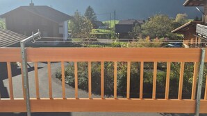 A wooden balcony with a view of a mountain and residential buildings. - Cozy vacation apartment - nature & relaxation (Aeschi bei Spiez)